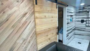 En modern inredning med en väggpanel i trä, en skjutdörr och en svart lädersoffa.
