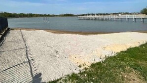 En betongbrygga som sträcker sig ut i ett stilla vattenområde, med en sandstrand i förgrunden.