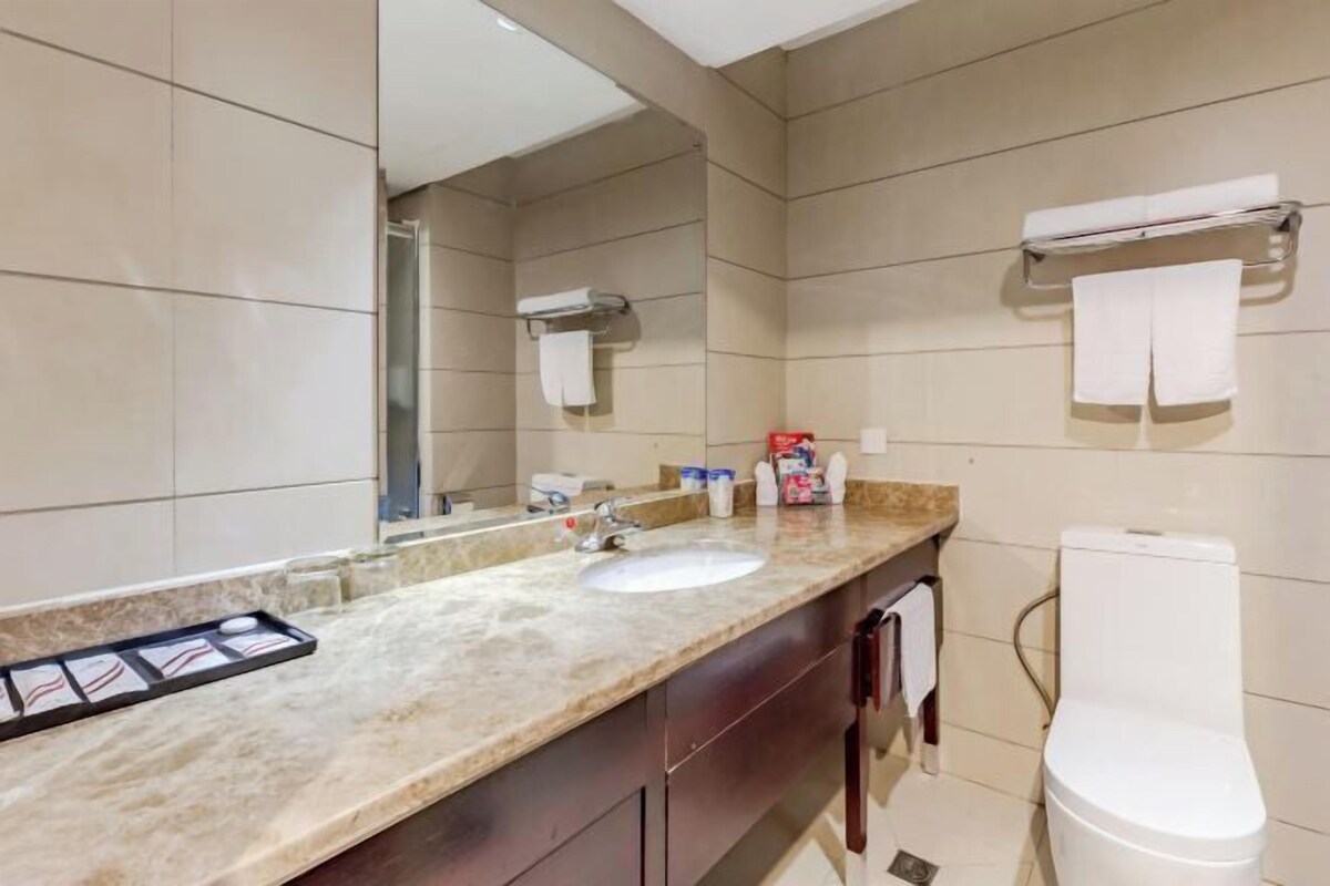 A modern bathroom with a marble countertop, a sink, a toilet, and a large mirror.