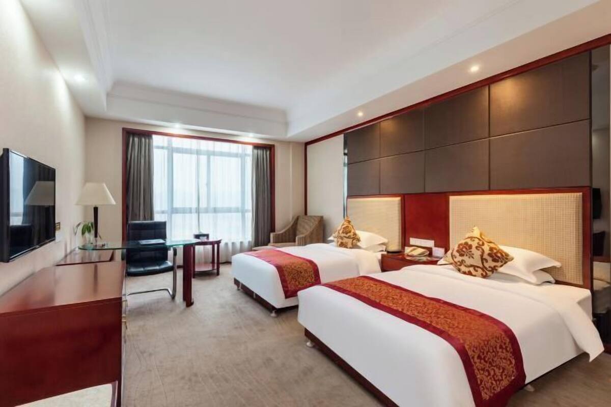 A hotel room with two beds, a desk, a chair, a TV, and a large window.