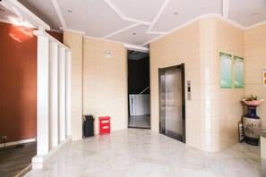 A hotel lobby with a marble floor, a reception desk, a red trash bin, and a wall-mounted information board. - Hongxing International Hotel (Jing County)