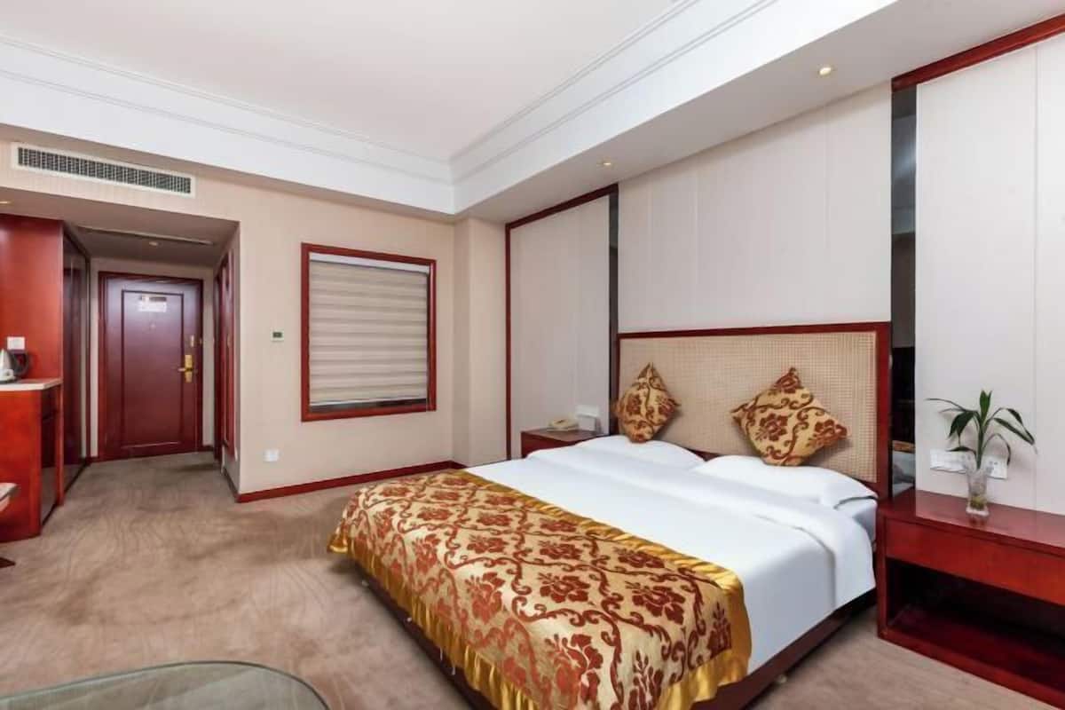 A hotel room with a bed, bedside table, lamp, and a door leading to another room.