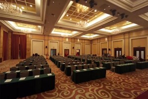 Une salle de conférence avec des rangées de tables et de chaises, une moquette à motifs et un lustre.