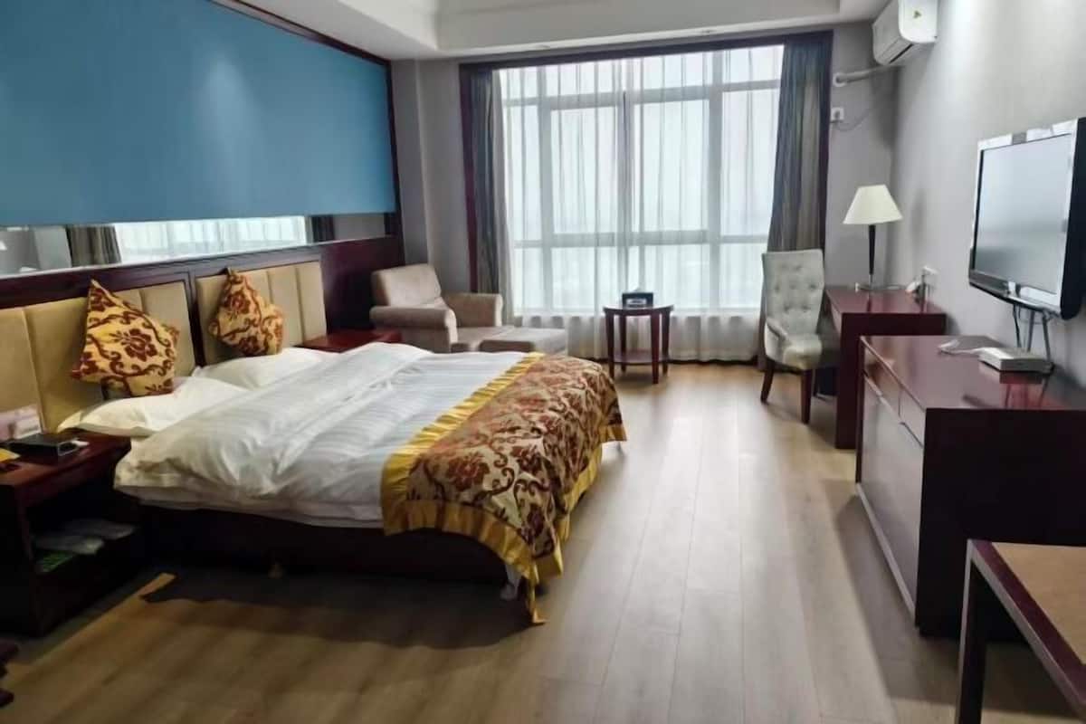 A hotel room with a bed, a desk, a chair, a TV, and a window with curtains.
