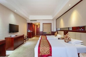 A hotel room with a large bed, a TV, a desk, and a minibar.