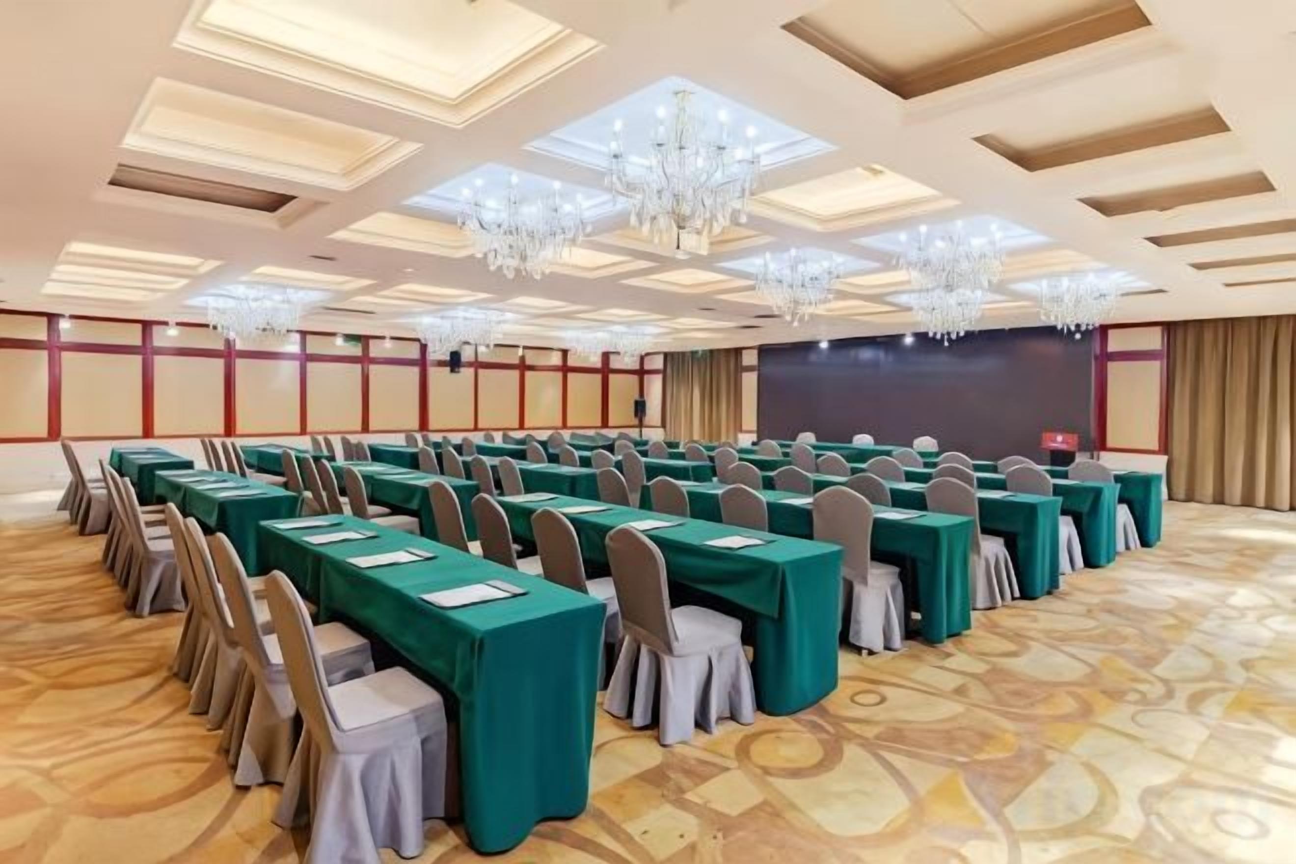 A conference room with rows of tables and chairs, a stage, and a large screen.