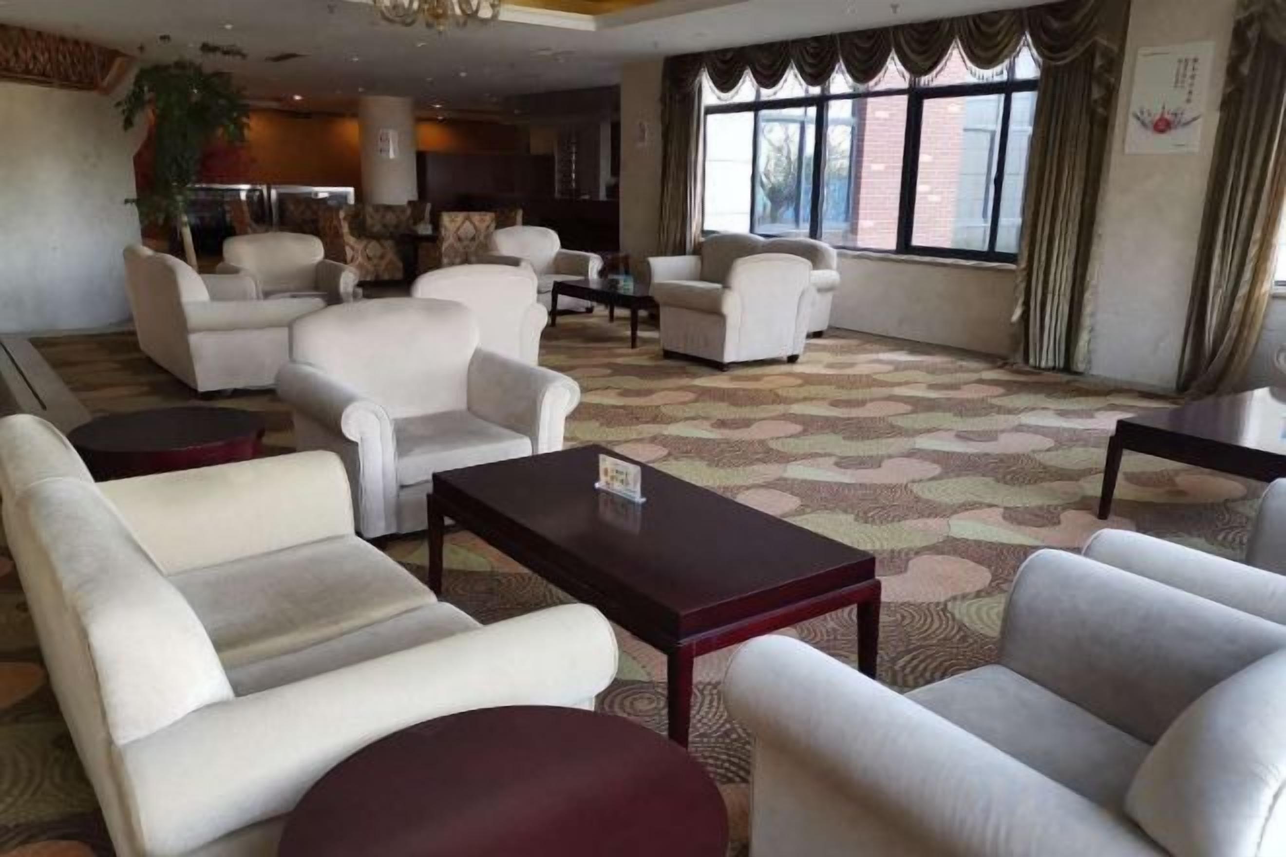 A hotel lobby with multiple seating areas, a large window with curtains, and a patterned carpet.