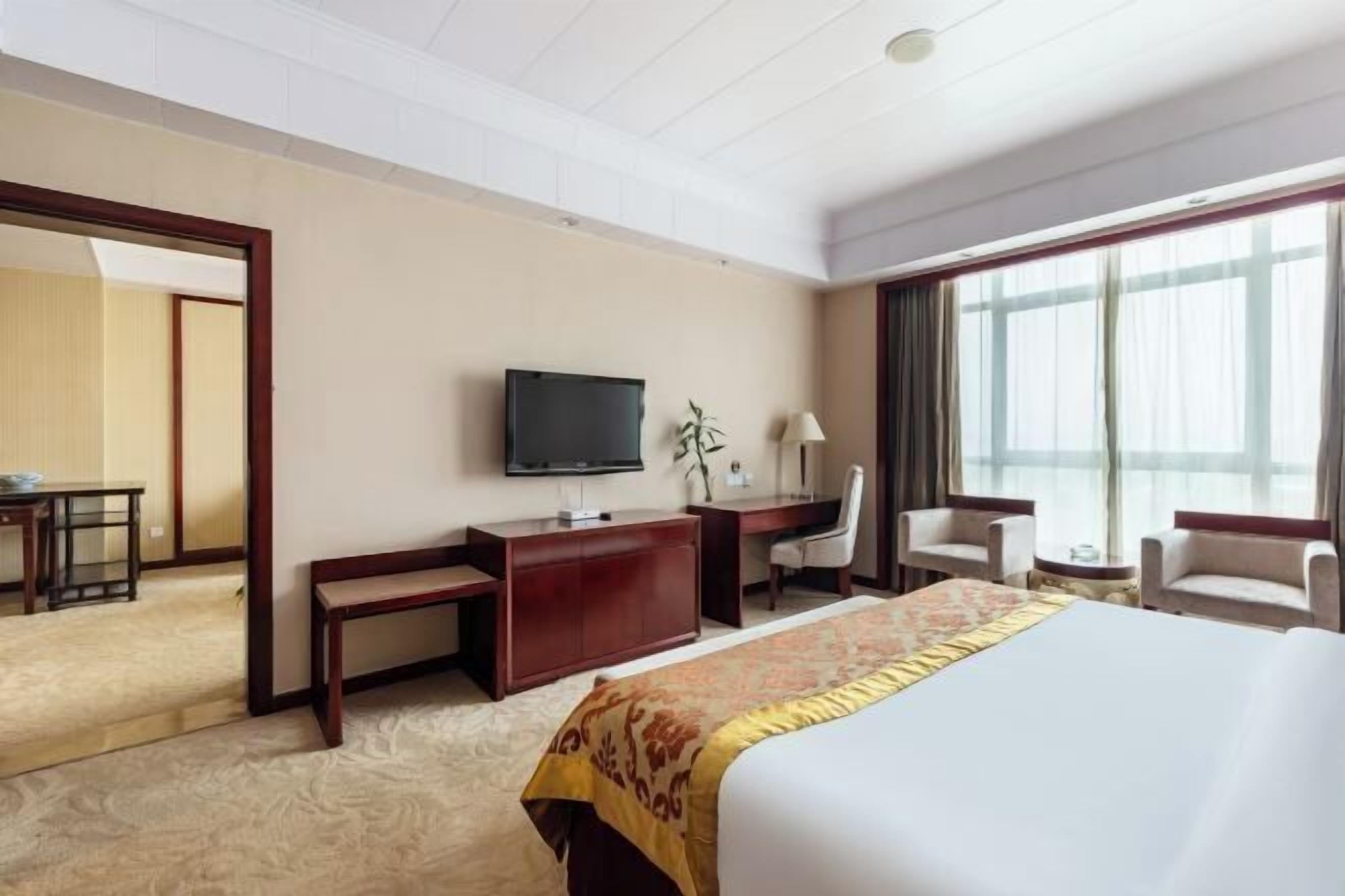 Une chambre d’hôtel avec un grand lit, un bureau, une télévision et deux chaises.
