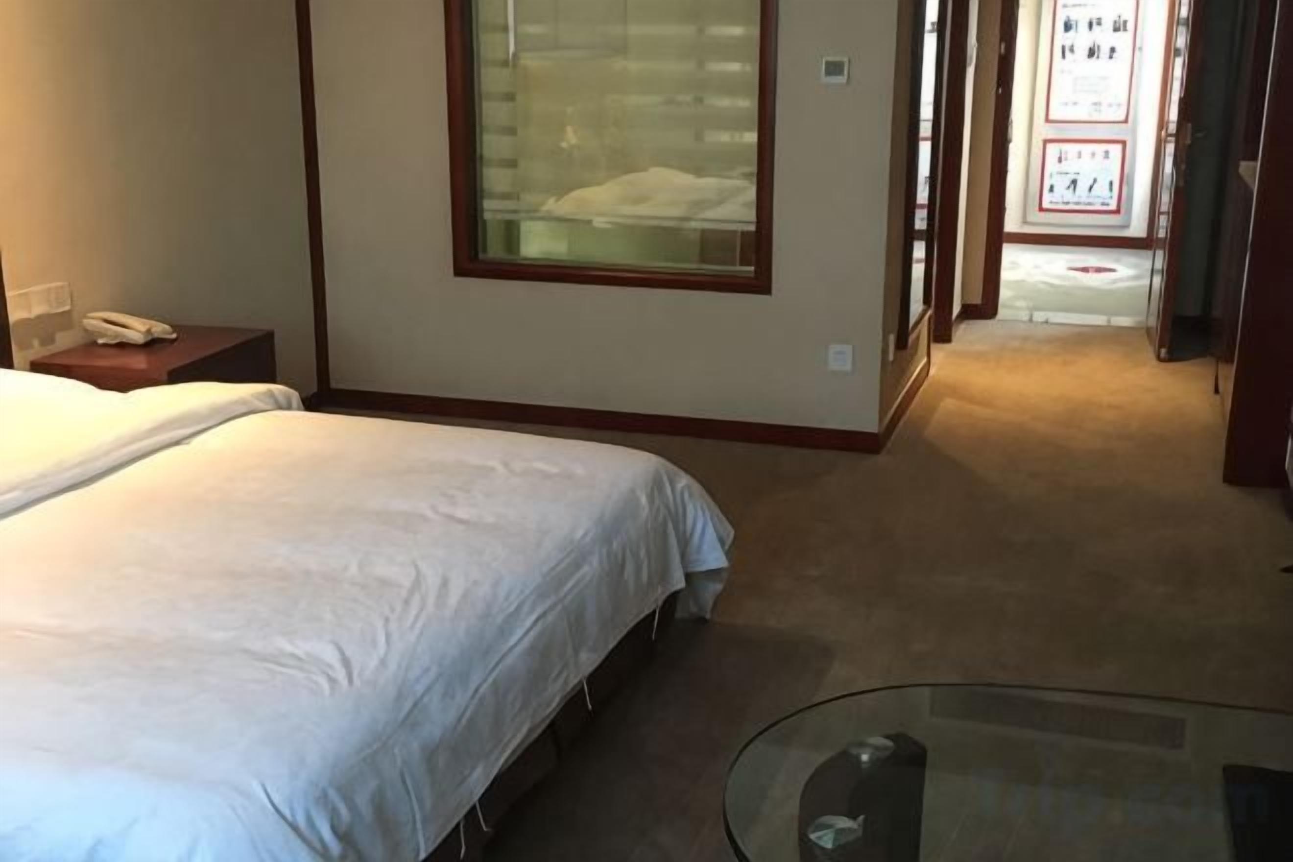 Habitación de hotel con cama, mesita de noche, una mesa de vidrio y vista al pasillo.