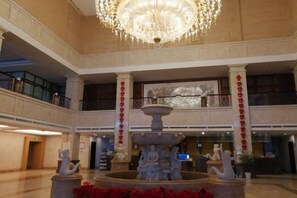 Un hall d’entrée spacieux, agrémenté d’un magnifique lustre, d’une fontaine centrale et d’un balcon décoré de rouge.