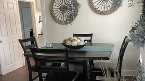 A dining room with a table set for four, surrounded by black chairs. There are two decorative wall pieces above the table. A vase with flowers is on the right side of the image. - Salisbury Bungalow (Salisbury)