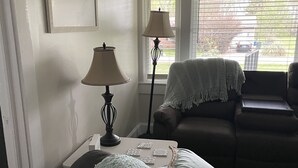 A living room with a couch, a table with a lamp, and a window with blinds. - Salisbury Bungalow (Salisbury)