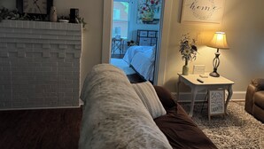 A cozy living room with a brick fireplace, a comfortable couch, and a small side table with a lamp and a sign. - Salisbury Bungalow (Salisbury)