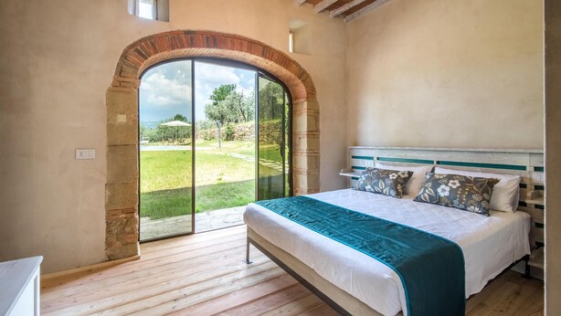 Un dormitorio con una cama grande, vistas a un jardín a través de un ventanal y un techo rústico.