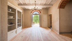 Un pasillo con suelo de madera, un candelabro y vistas al exterior con vegetación.