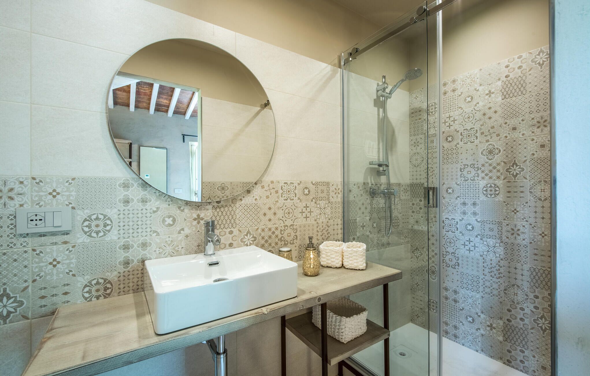 A bathroom with a round mirror, a sink, and a shower area.