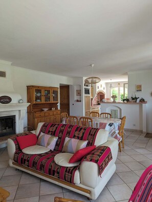 A living room with a sofa, a fireplace, a dining area with a table and chairs, and a kitchen area with a counter and cabinets.