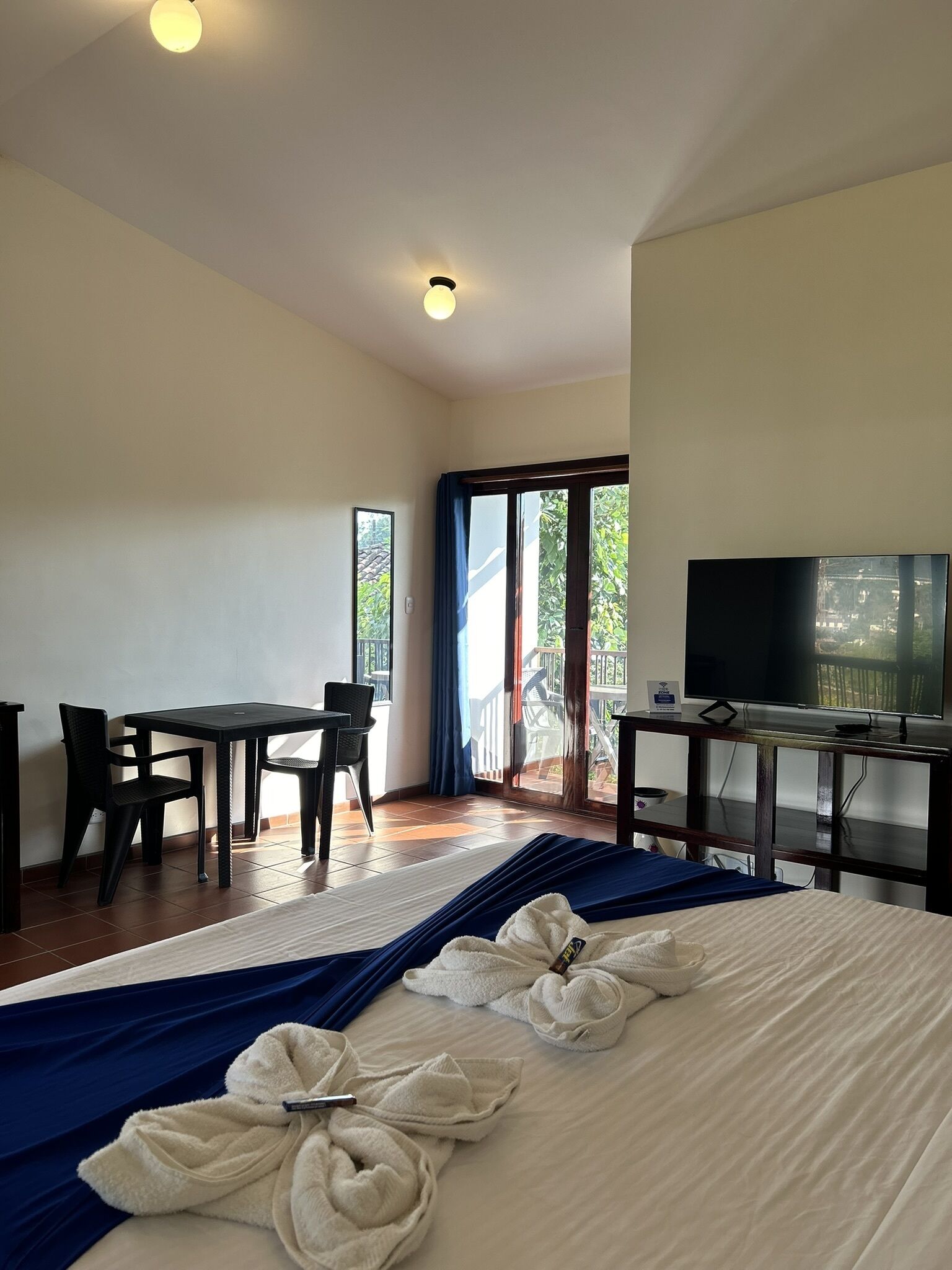 A hotel room with a bed, a TV, a desk with chairs, and a balcony with a view.