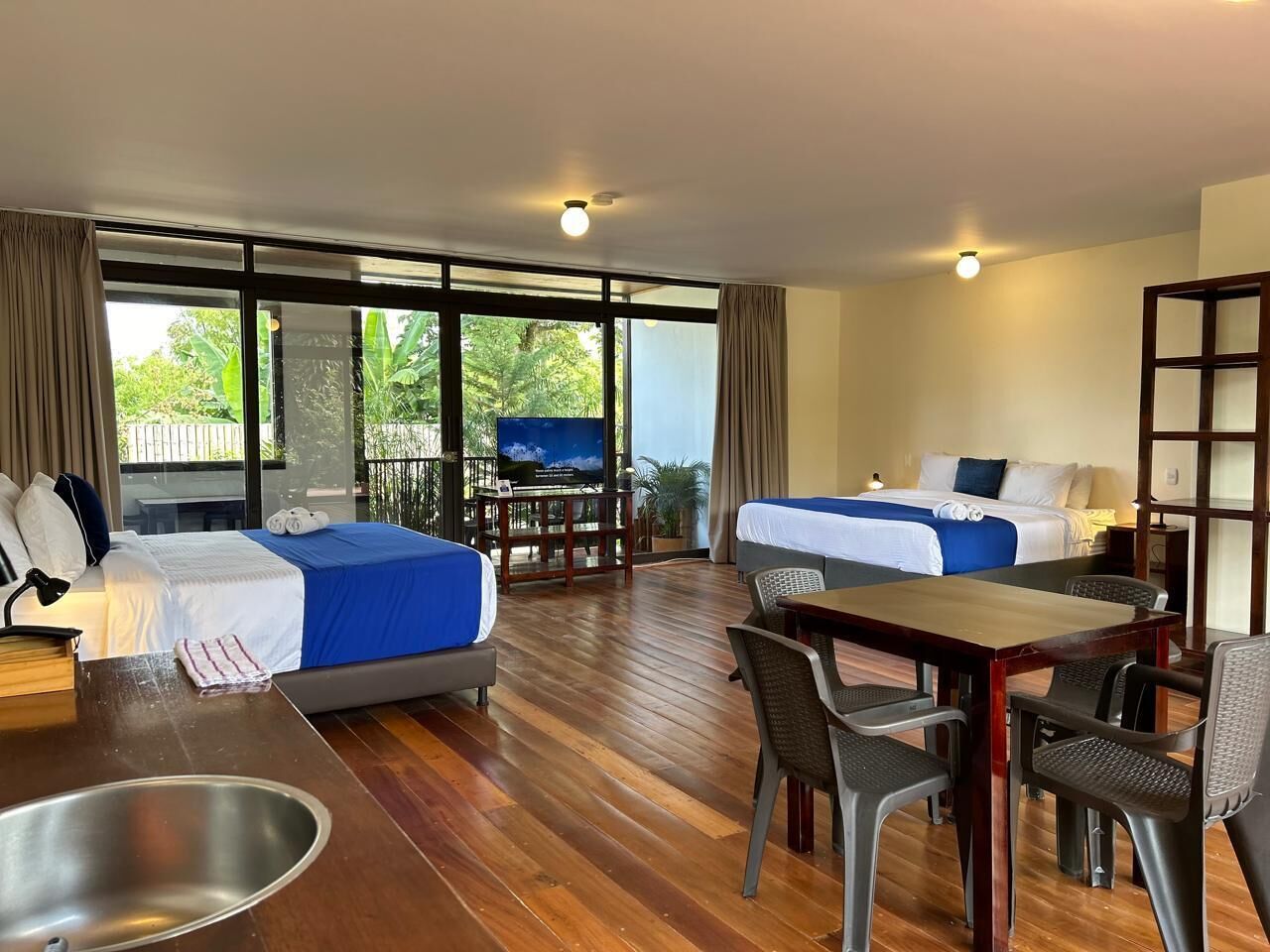 Habitación de hotel con dos camas, una mesa de comedor y un televisor.
