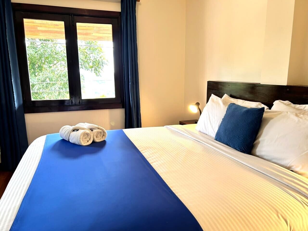 Une chambre d’hôtel avec un lit, une table de chevet, une lampe et une fenêtre avec des rideaux.
