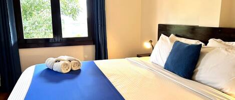 A hotel room with a bed, a nightstand, a lamp, and a window with curtains.