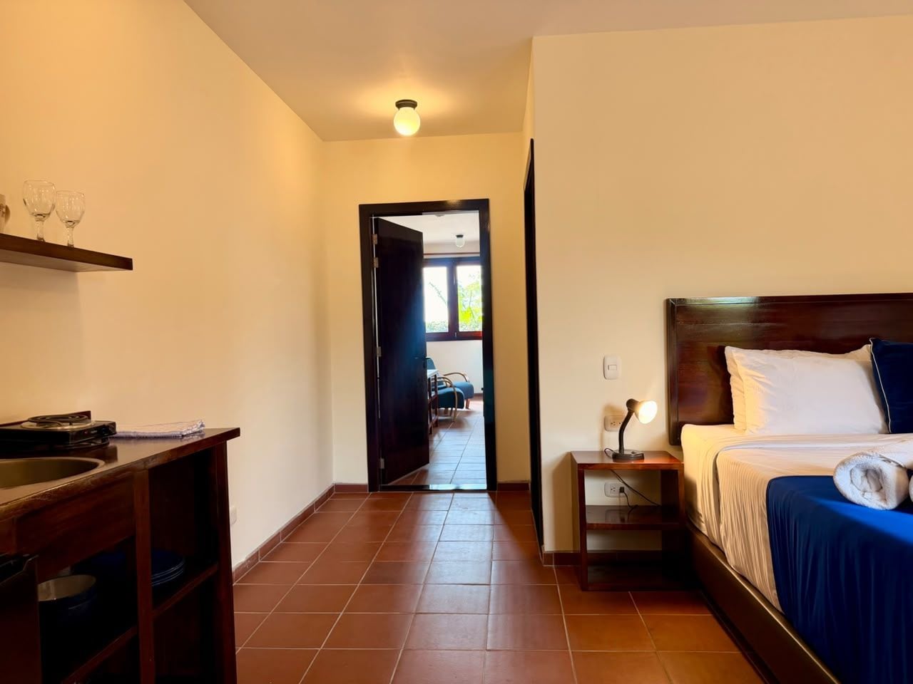 Ein Hotelzimmer mit Bett, Nachttisch und Blick durch eine offene Tür auf einen Balkon.