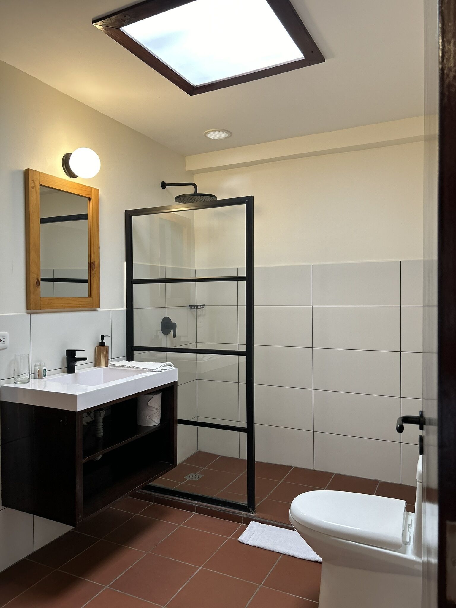 A modern bathroom with a skylight, a glass shower enclosure, a white sink, and a toilet.