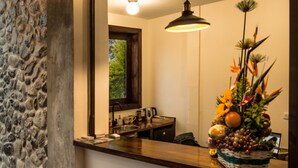 Cocina con pared de piedra, techo de madera y un espejo grande que refleja un lámpara colgante y un arreglo floral.