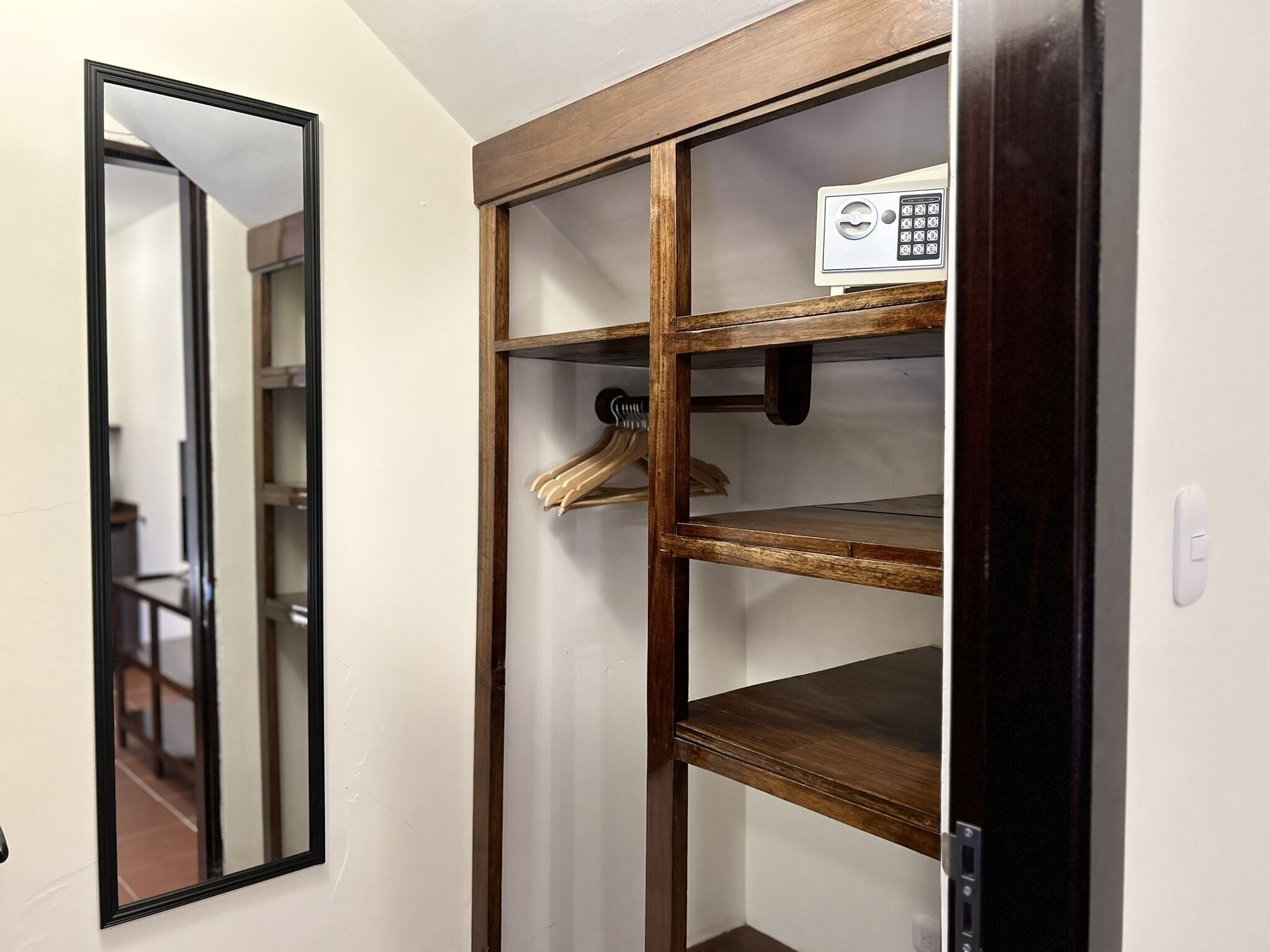 Une armoire en bois dotée de plusieurs étagères et d’une tringle pour suspendre les vêtements, ainsi que d’un miroir et d’un petit panneau de commande situé sur l’étagère supérieure.