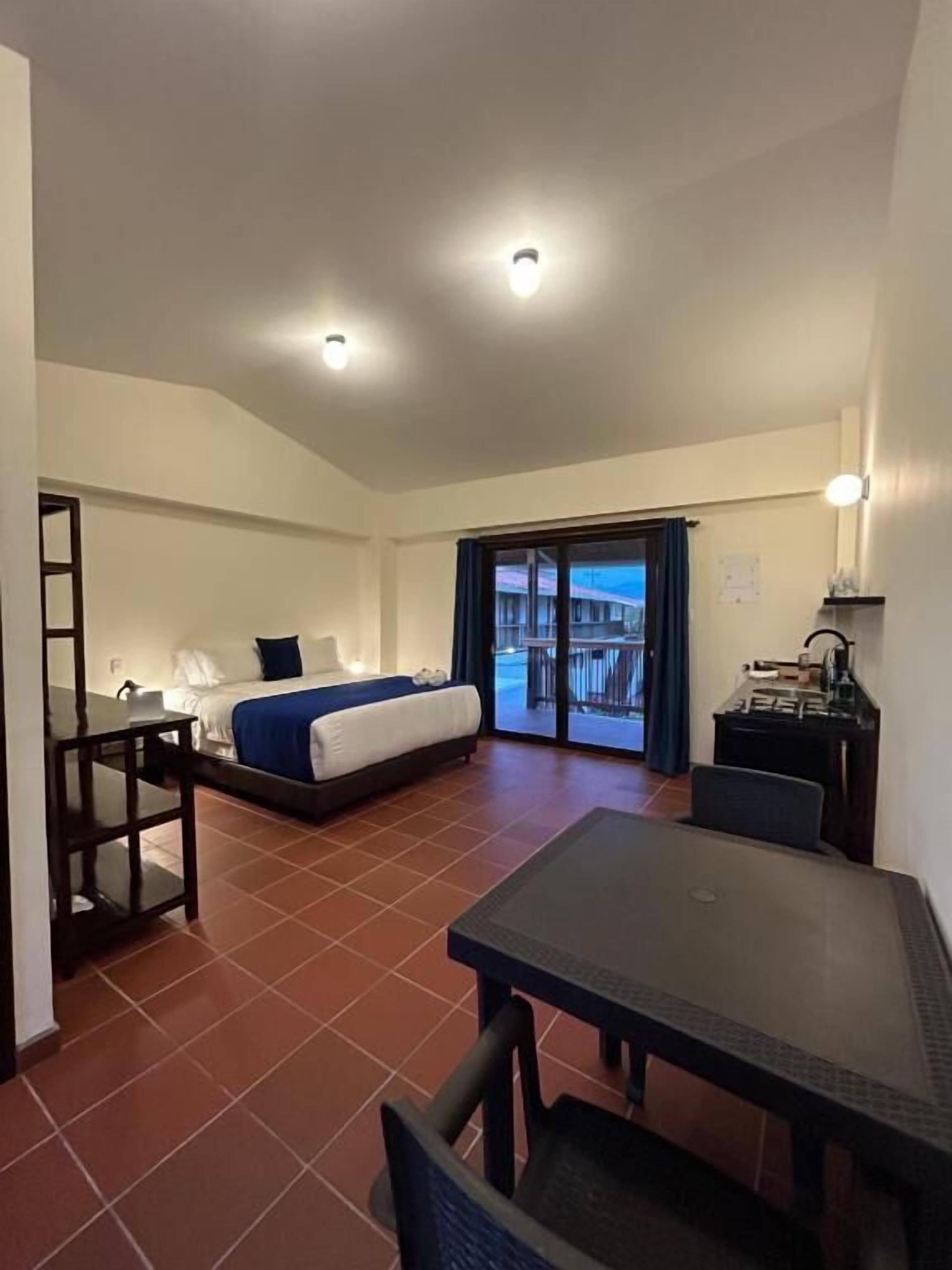 Habitación de hotel con cama, escritorio, silla y mesa. Tiene un balcón con vistas al exterior.