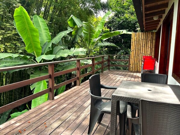 A wooden deck with a table and chairs, surrounded by lush greenery. - Villa Salento Boutique Apartments (Salento)