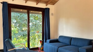 Una habitación con techo de madera, un sofá azul, un sillón azul y un amplio ventanal corredero que da a un jardín.