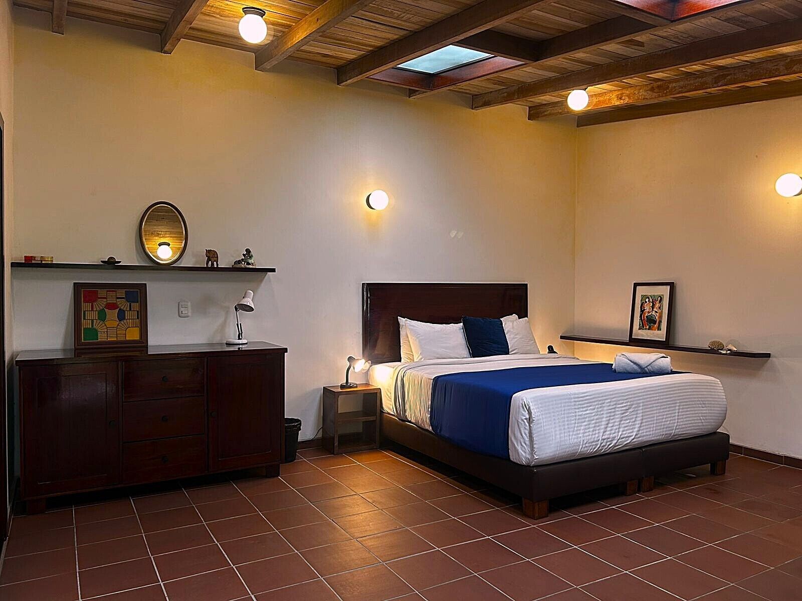 A bedroom with a bed, bedside tables, a dresser, and wall-mounted lighting.