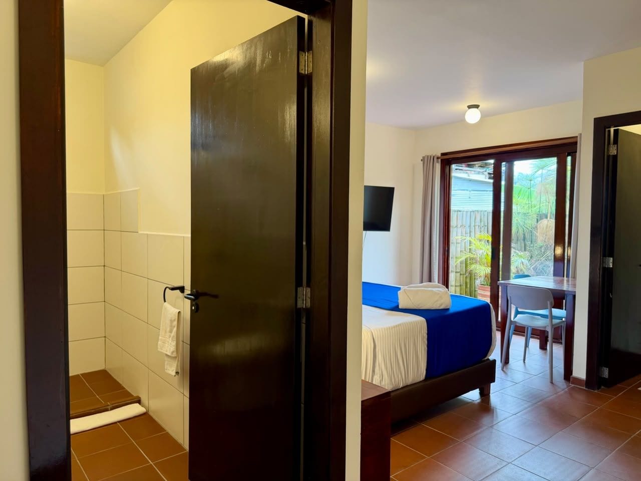 Een hotelkamer met douche, een bed met een blauwe hoes, een tafel met een stoel en een balkon met uitzicht.