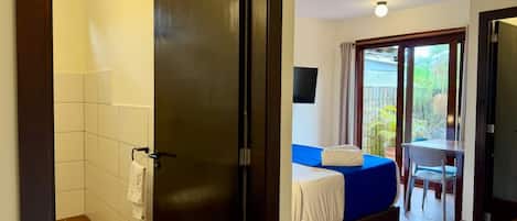 Een hotelkamer met douche, een bed met een blauwe hoes, een tafel met een stoel en een balkon met uitzicht.