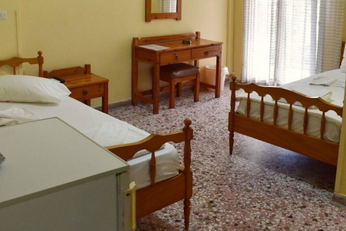 A room with two wooden beds, a wooden desk, a chair, a mirror, and an air conditioning unit.