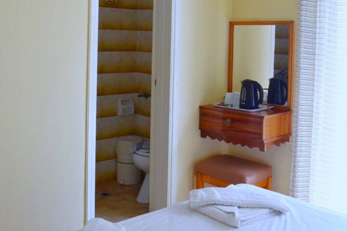 A hotel room with a bed, a television mounted on the wall, a bathroom with a shower curtain, and a small wooden table with a kettle and cups.