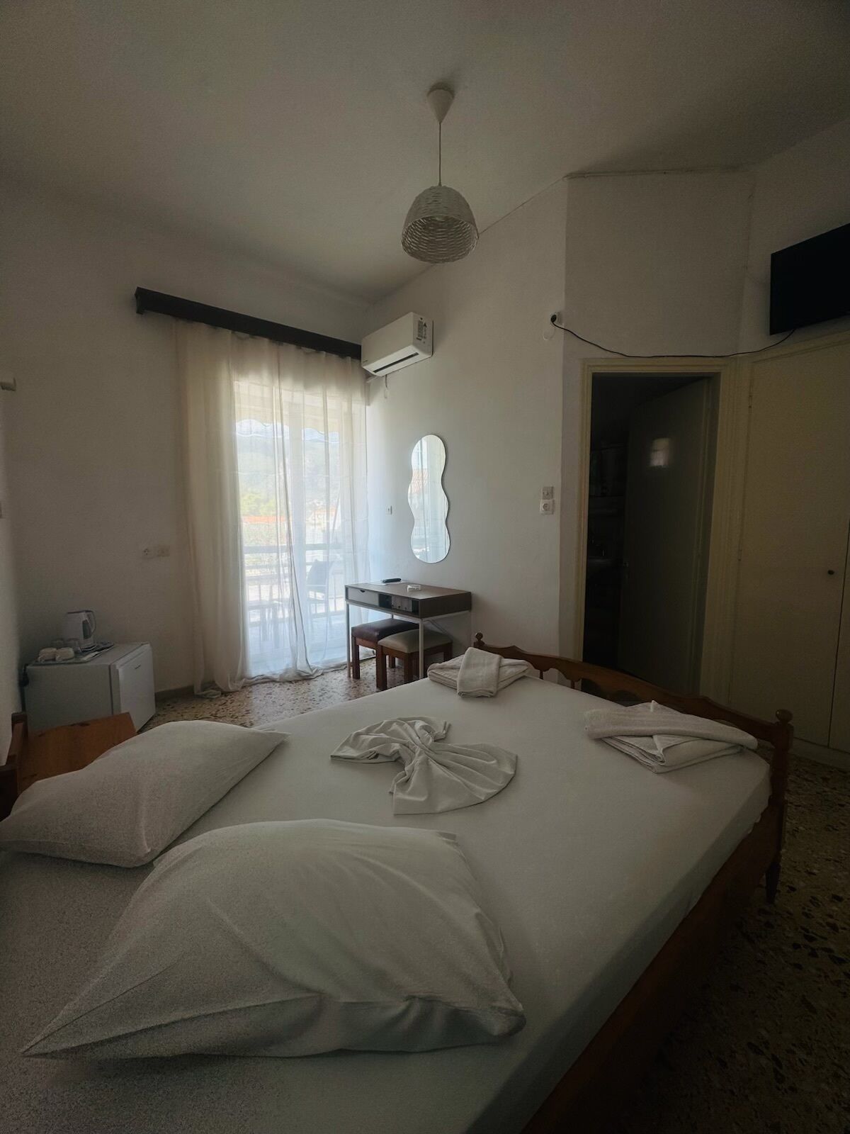 A hotel room with a bed, a desk, a chair, an air conditioning unit, and a television on the wall.