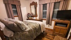 Une chambre à coucher avec un lit, un téléviseur posé sur un meuble en bois, un miroir et une petite table sur laquelle se trouve un vase de fleurs.