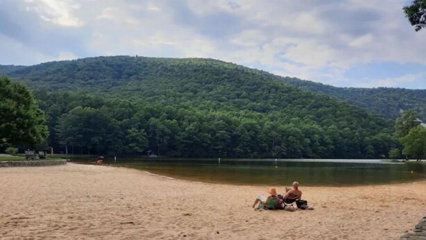 Une plage de sable bordée d’un lac, avec des collines boisées en arrière-plan.
