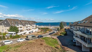 Una zona residenziale costiera con edifici moderni, una strada con auto parcheggiate e una vista aperta sul mare.