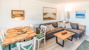 Un soggiorno con un tavolo da pranzo in legno, un divano e un tavolino. Alle pareti ci sono dei quadri e una lampada a sospensione.