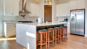 Een moderne keuken met witte kasten, een roestvrijstalen koelkast en een centraal eiland met barstoelen.