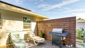 Un patio exterior con una parrilla, dos sillones de descanso y una valla de madera.