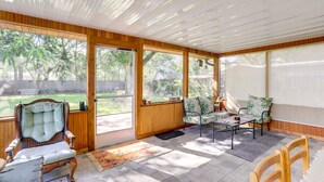 Un patio cubierto con paredes de madera, ventanas amplias y una variedad de asientos, incluyendo una butaca acolchada, un sofá y una mesa.