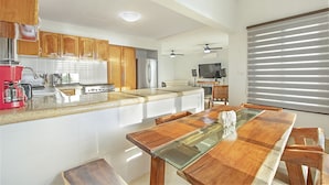 A modern kitchen with wooden cabinets, a stainless steel refrigerator, a red coffee maker, and a glass-top dining table. - Casa Kauil, an oceanfront villa in Celestun (Celestún)