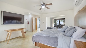 A bedroom with a bed, a wooden bench, a ceiling fan, and a TV mounted on the wall. - Casa Kauil, an oceanfront villa in Celestun (Celestún)