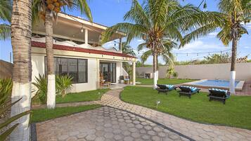 Ein zweigeschossiges Haus mit Swimmingpool, Palmen und einer sechseckig gefliesten Terrasse.