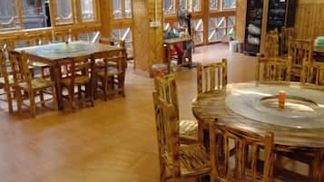 A wooden interior with round tables and chairs, a fan, and a refrigerator.