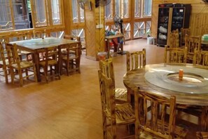 A wooden interior with round tables and chairs, a fan, and a refrigerator. - Dongzhai Xiangfeng Inn (Sanjiang)